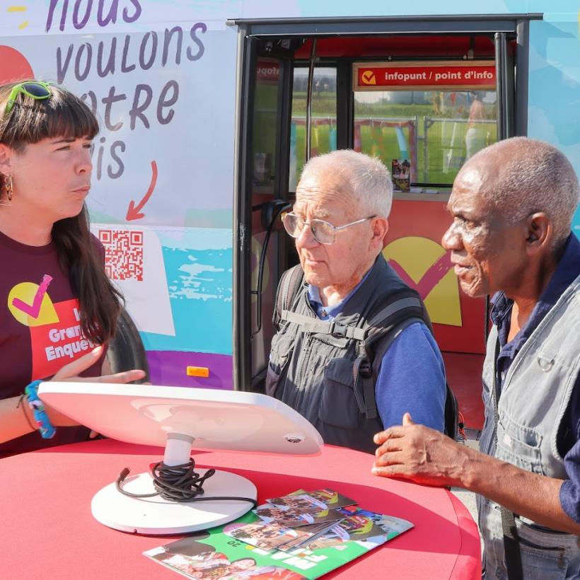 Une bénévole du PTB fait remplir la Grande Enquête à deux passants.