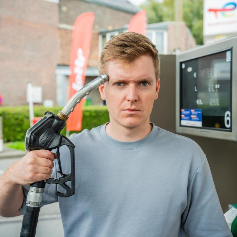 Un homme à une station-service tient le pistolet de la pompe contre sa tête et regarde avec colère.