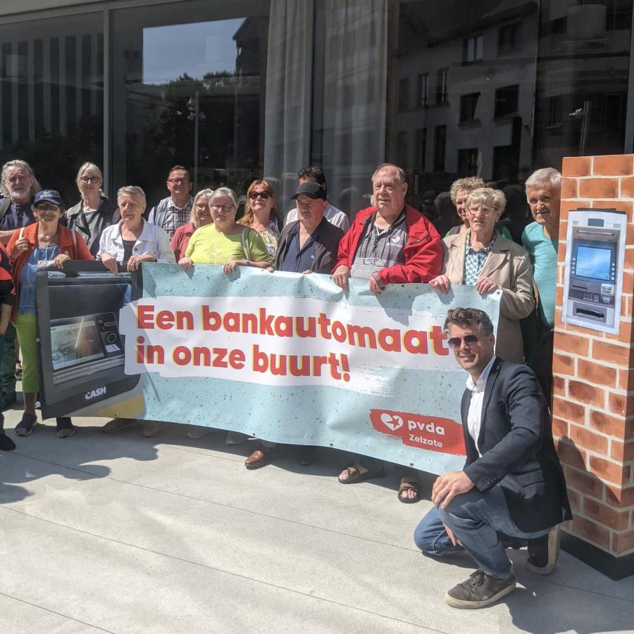 Foto van een PVDA-groep met een spandoek dat een geldautomaat in de buurt eist.