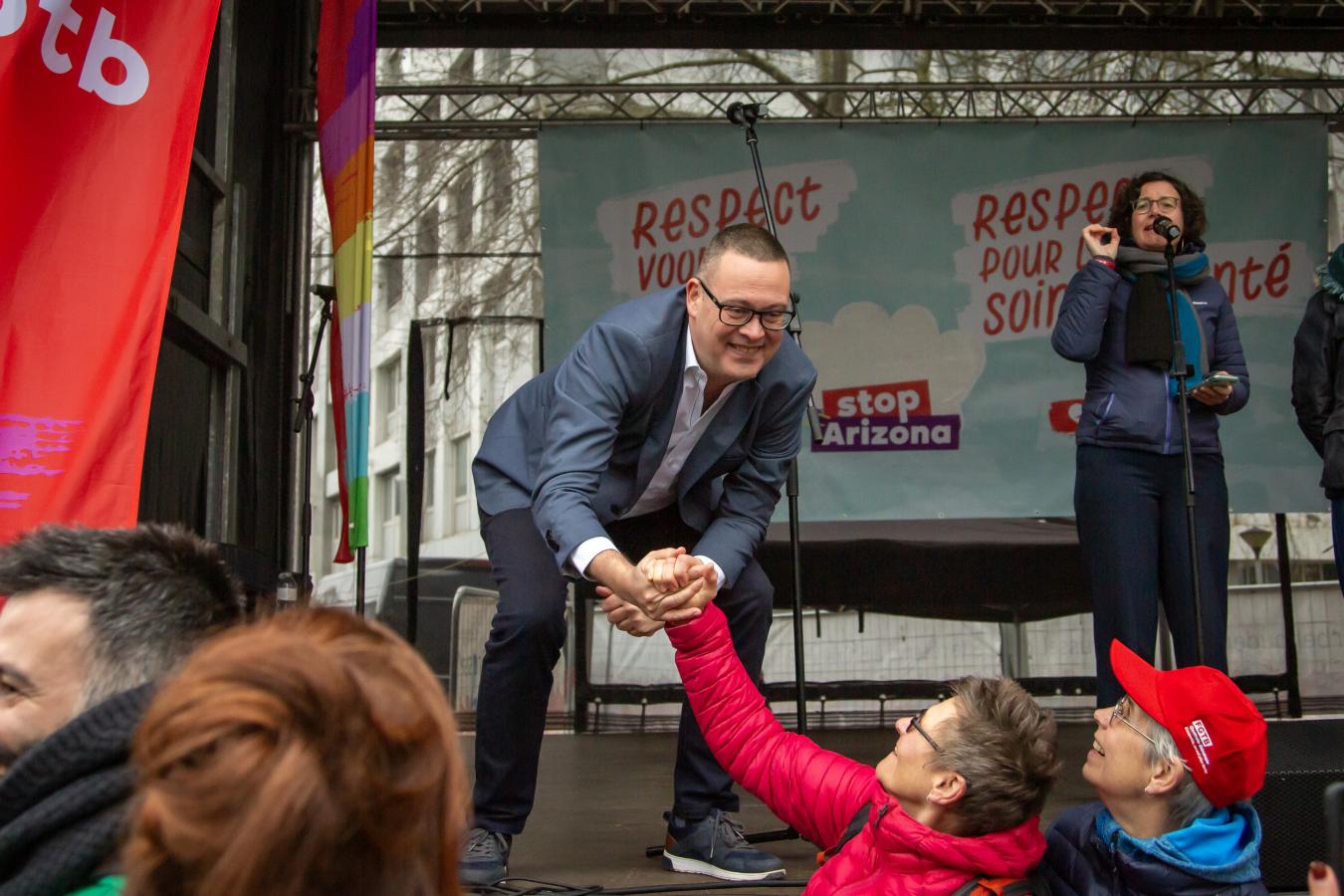 Raoul Hedebouw sert la main à des manifestants depuis un podium lors de la manifestation du non-marchand.