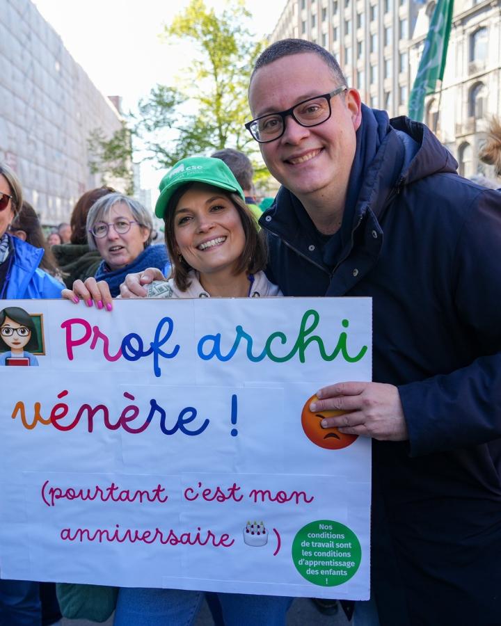 Raoul Hedebouw pose avec une affiche "Prof archi vénère" et une syndicaliste CSC à la manifestation des enseigants à Liège