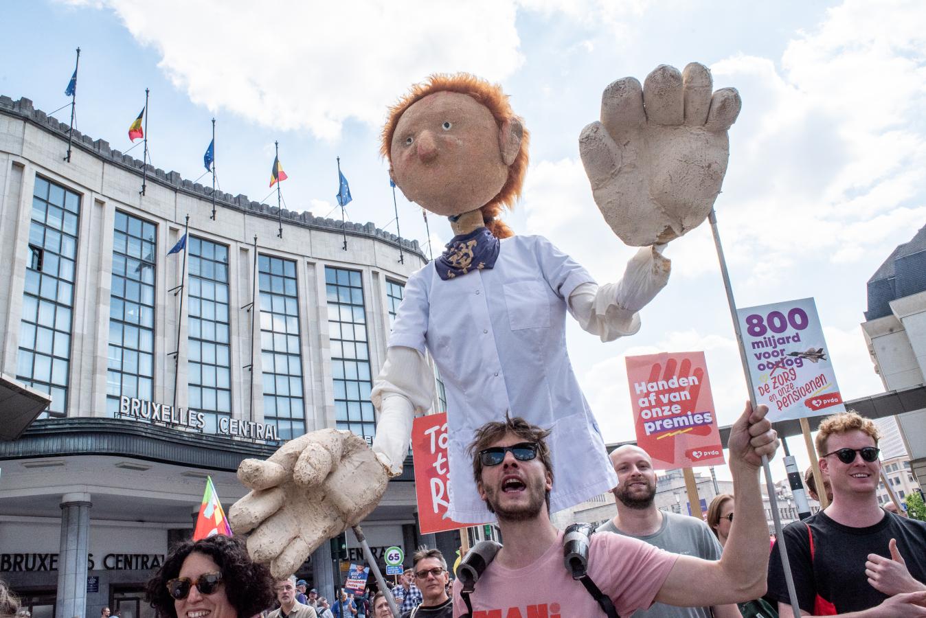 Un homme porte une grande marionette avec une blouse blanche sur le dos.