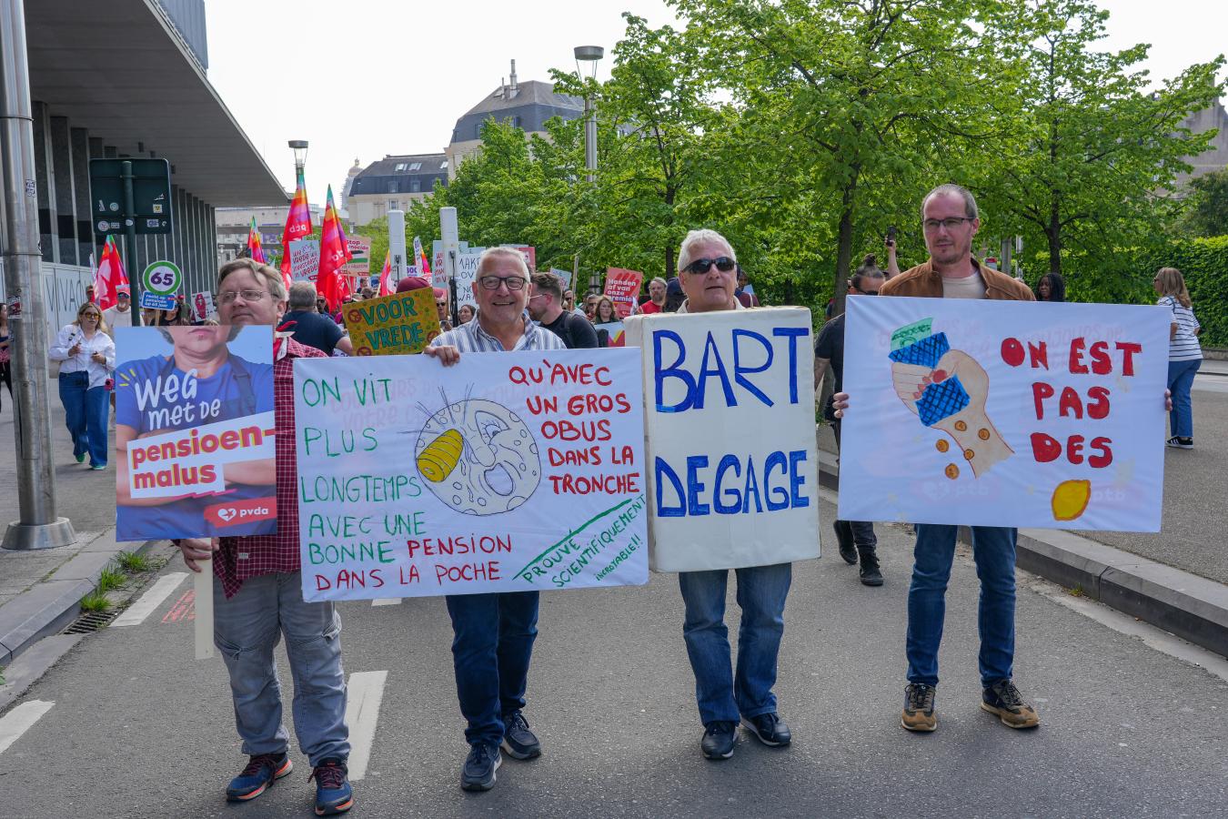Photo de groupe de 4 hommes avec des pancartes : "On vit plus longtemps avec une bonne pension qu'avec un gros obus dans la tronche", "Bart dégage" et "On n'est pas des citrons"