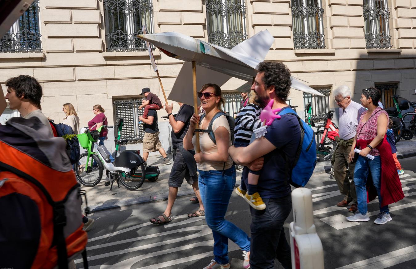 Une famille marche en portant un avion en carton au bout d'un bâton