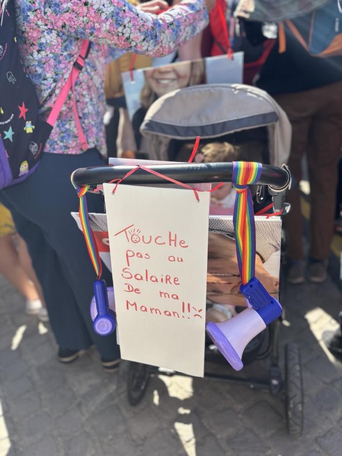 Une pancarte accrochée à une poussette : "Touche pas au salaire de ma maman"