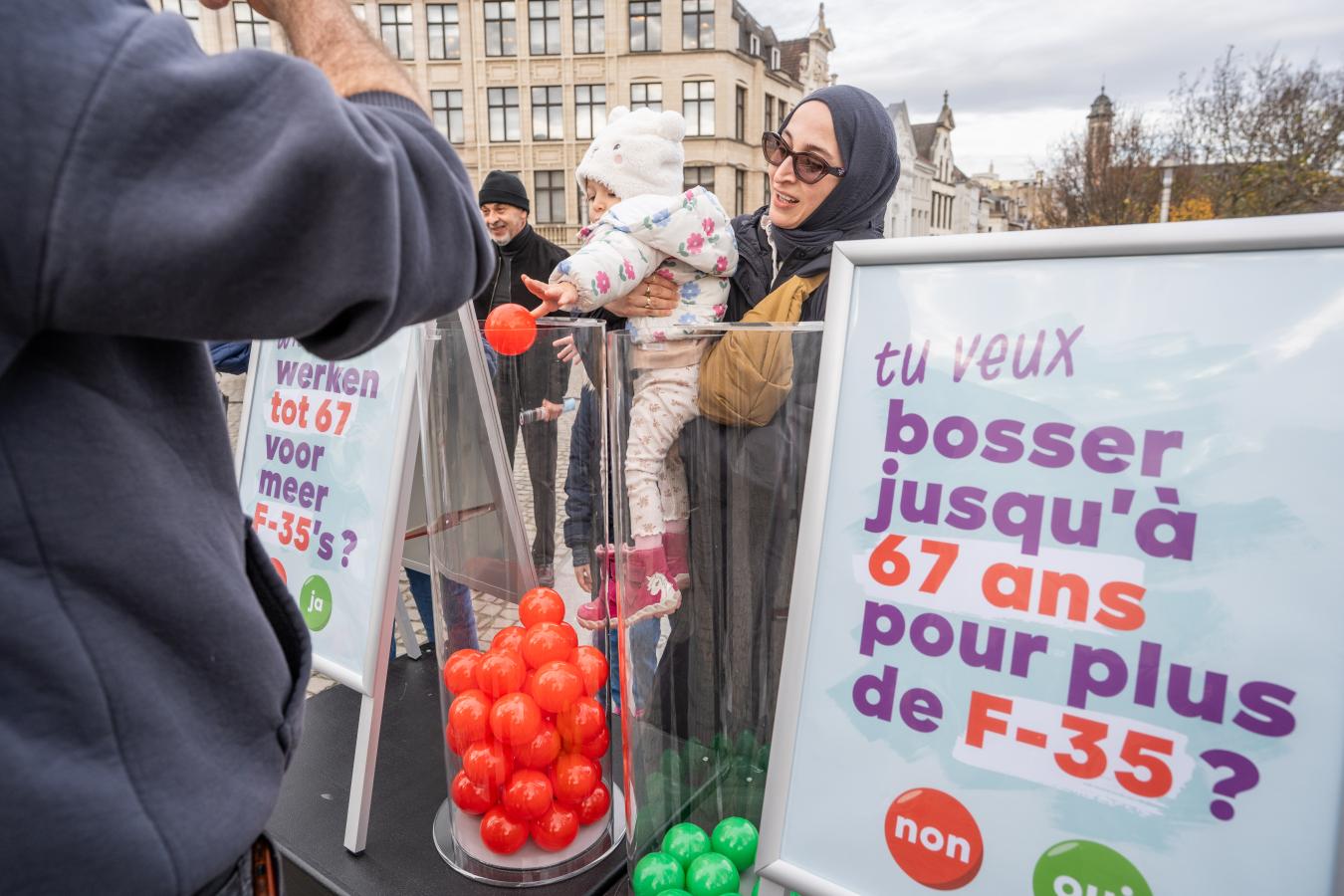 Une maman porte son enfant pour placer une boule rouge dans le bac "non" pour voter sur la question "Tu veux bosser jusqu'à 67 ans pour plus de F-35 ?"