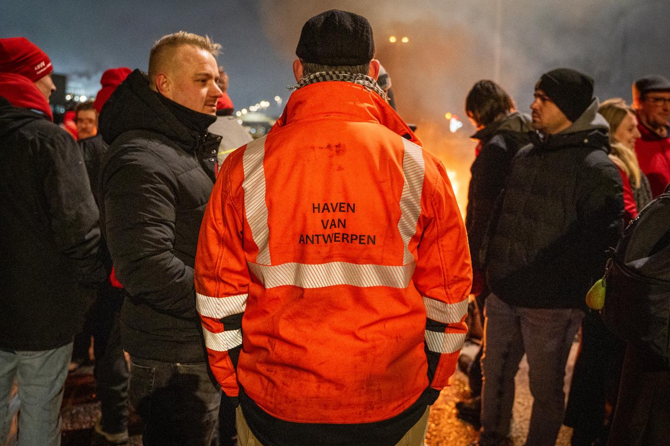 Un travailleur en grève de dos, avec écrit "port d'Anvers" sur sa veste