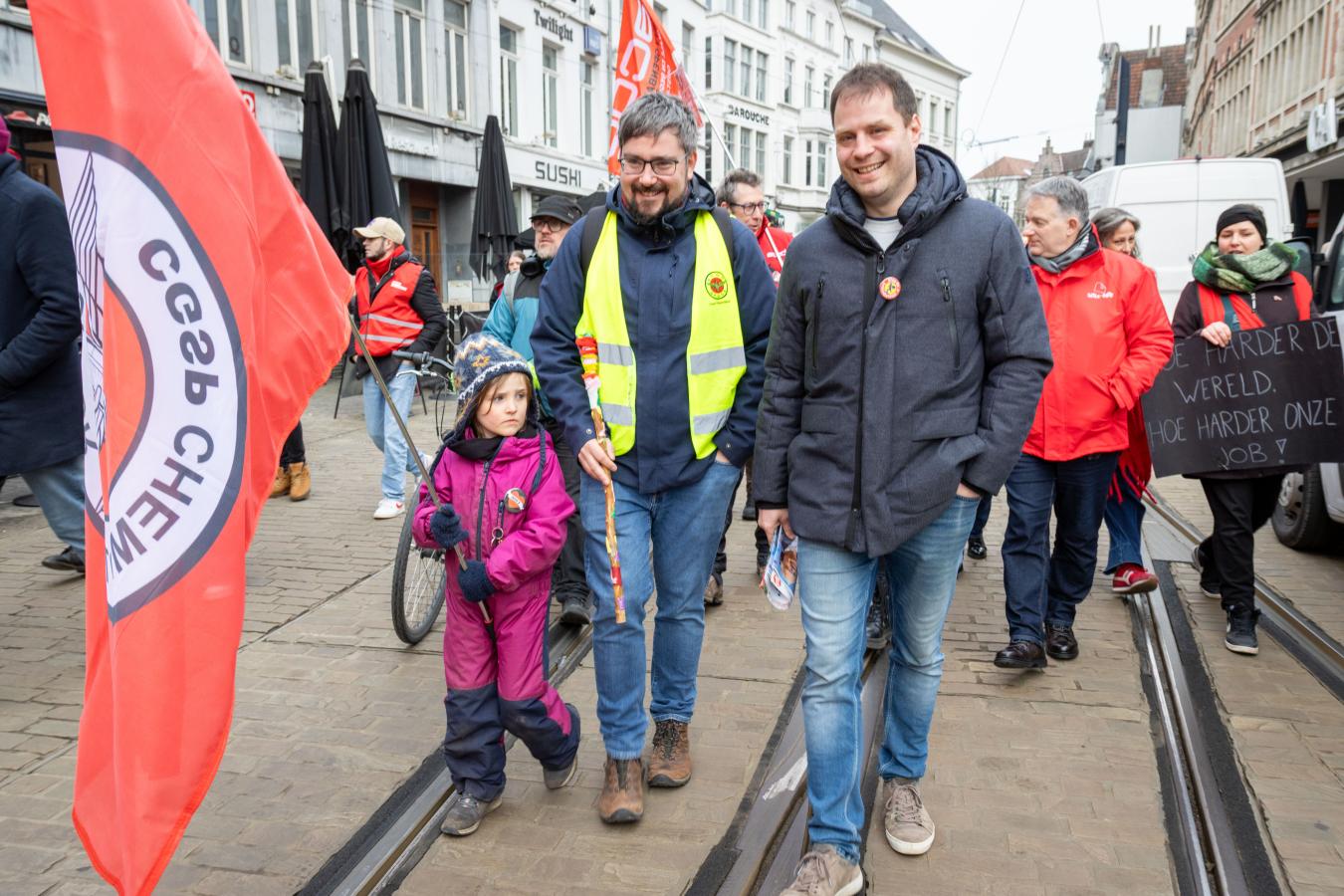 Deux hommes et une enfant tenant un drapeau défilent à Gand pour la journée d'actions du 5 février 2026
