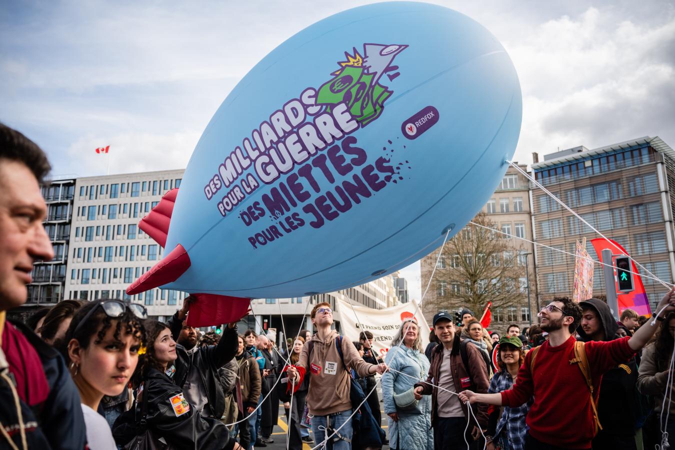 Un ballon en forme de missile sur lequel est écrit "Des milliards pour la guerre, des miettes pour les jeunes"