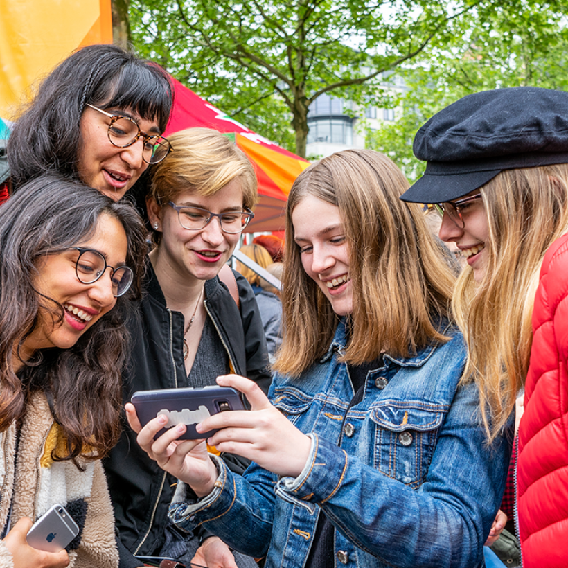 Cinq jeunes personnes regardent un smartphone avec un air enthousiaste.