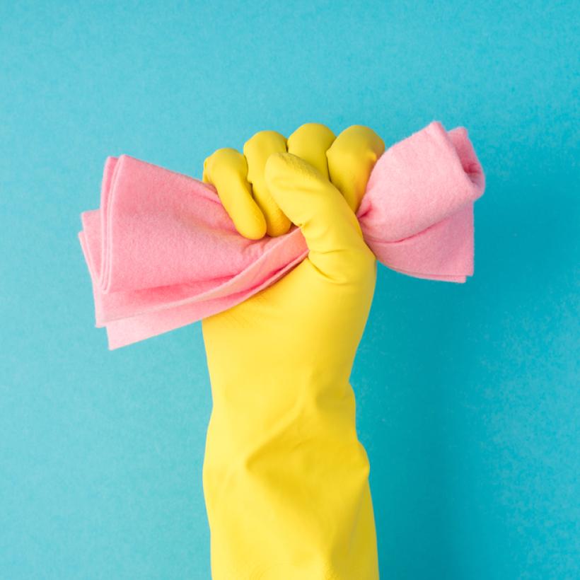 Een hand in een schoonmaakhandschoen houdt een spons in de vuist gekneld