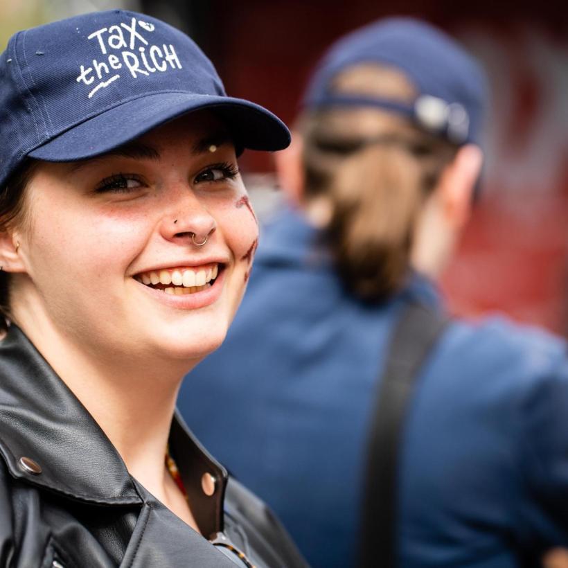Photo d'une jeune femme souriante avec une casquette "Tax the rich"