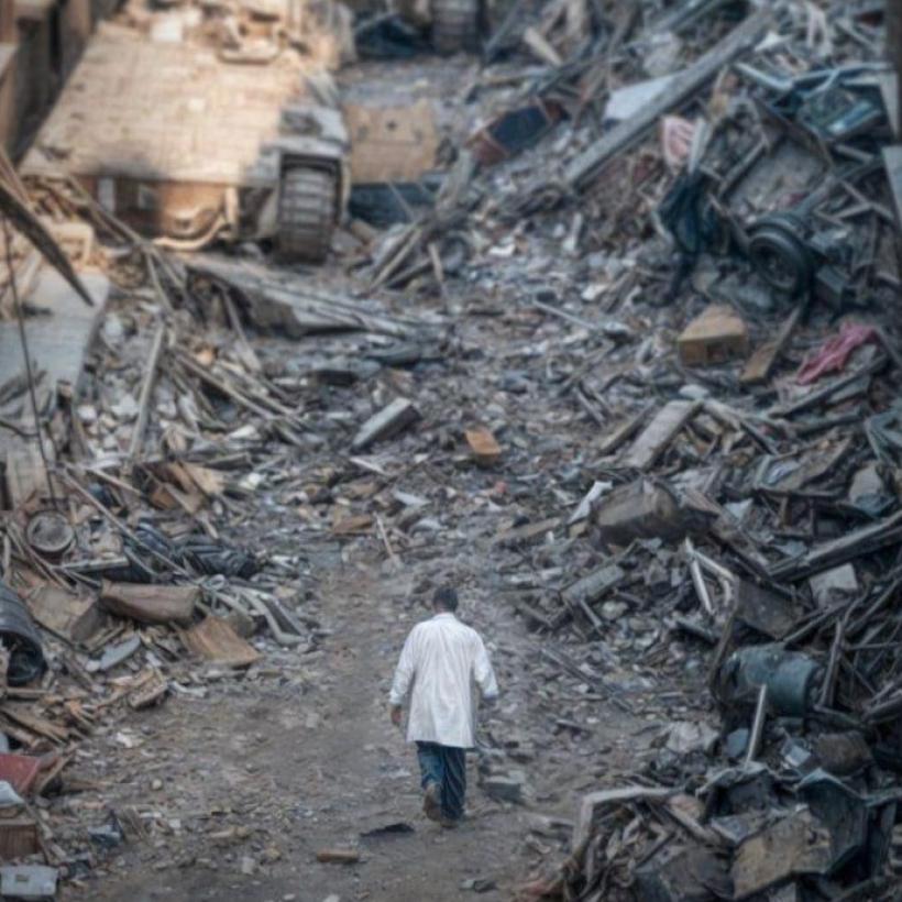 Image du Dr Hussam Abu Safiya marchant parmi les décombres des bâtiments détruits, avec un tank israélien à l'arrière-plan.