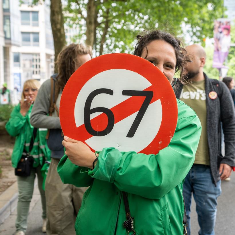 Une manifestante tient un panneau avec le nombre 67 barré. 