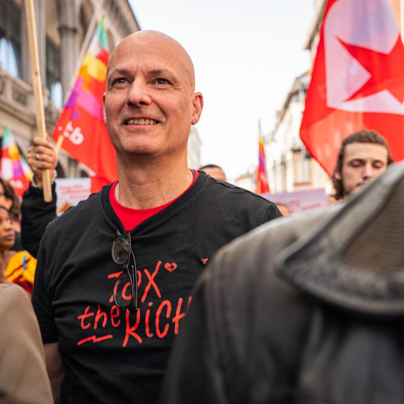 Un homme au milieu d'une manifestation avec un T-shirt « Tax The Rich ».