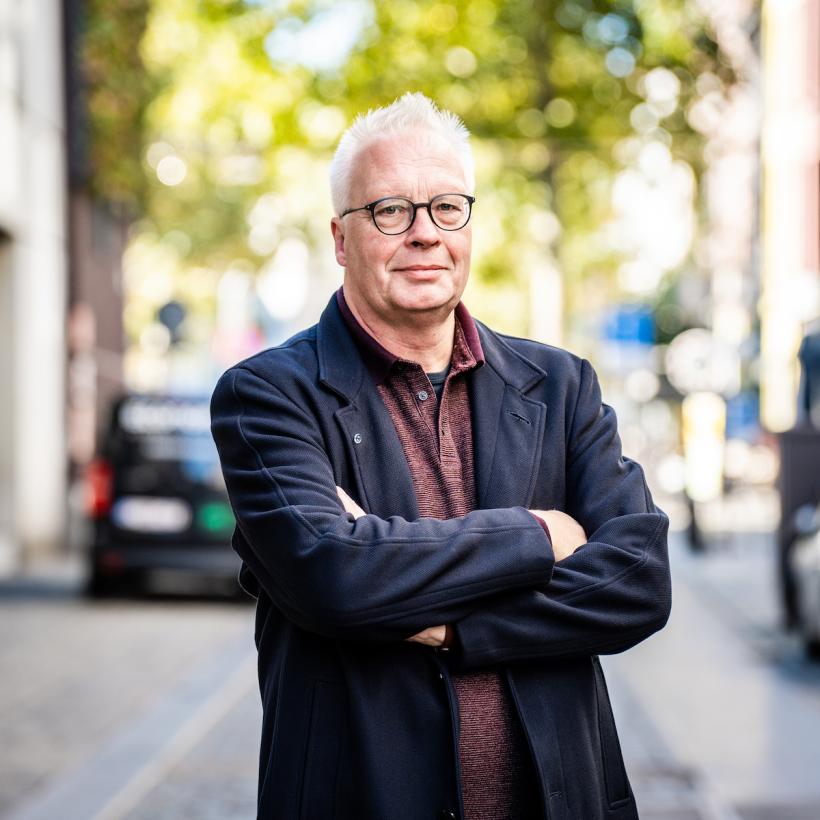 Peter Mertens met gekruiste armen in een straatbeeld