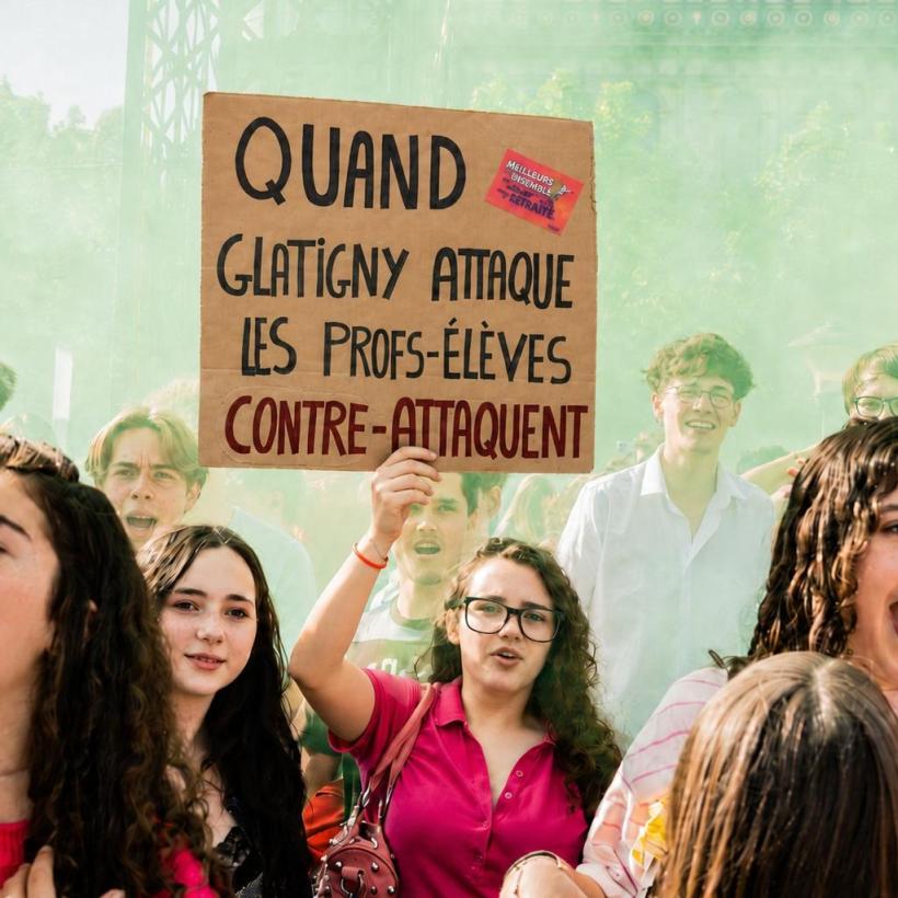 Une jeune parmi la foule portant une affiche "Quand Glatigny attaque, les profs-élèves contre-attaquent"