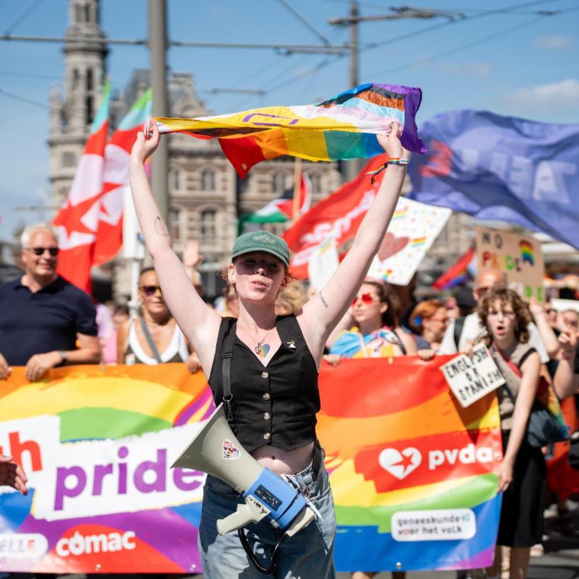 Un cortège du PTB lors d'une marche des fiertés, avec en tête une personne brandissant le drapeau arc-en-ciel