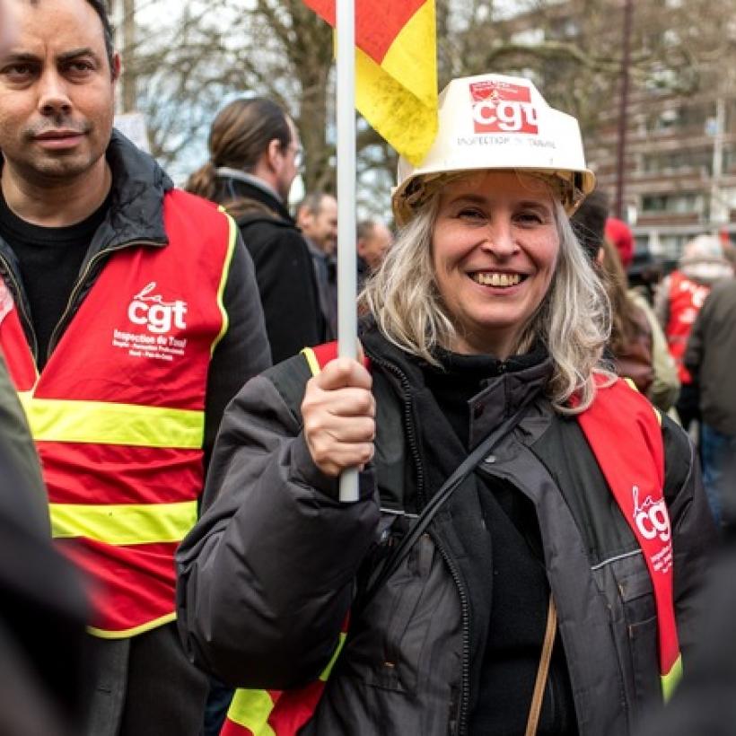 Une femme manifeste avec un casque et une veste portant le logo de la CGT.