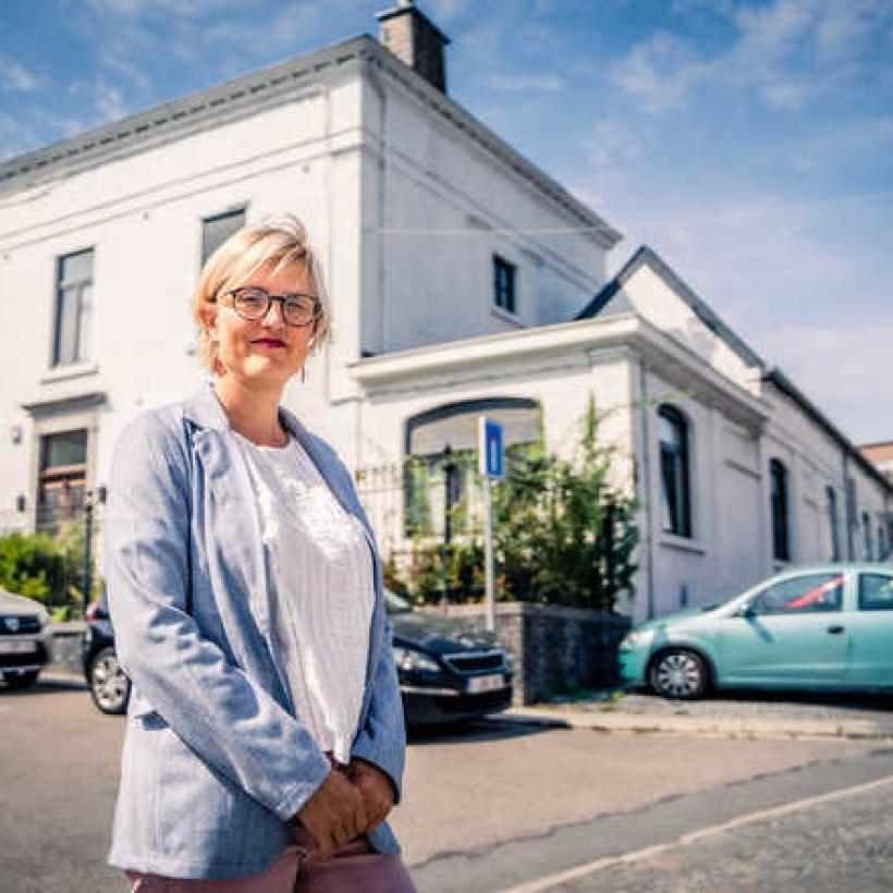 Sofie Merckx devant un bâtiment blanc à l'extérieur. Elle porte une tenue estivale.