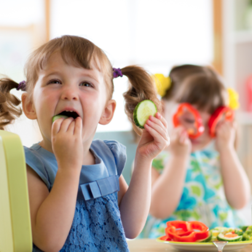 Une petite fille mange des légumes à l'école.