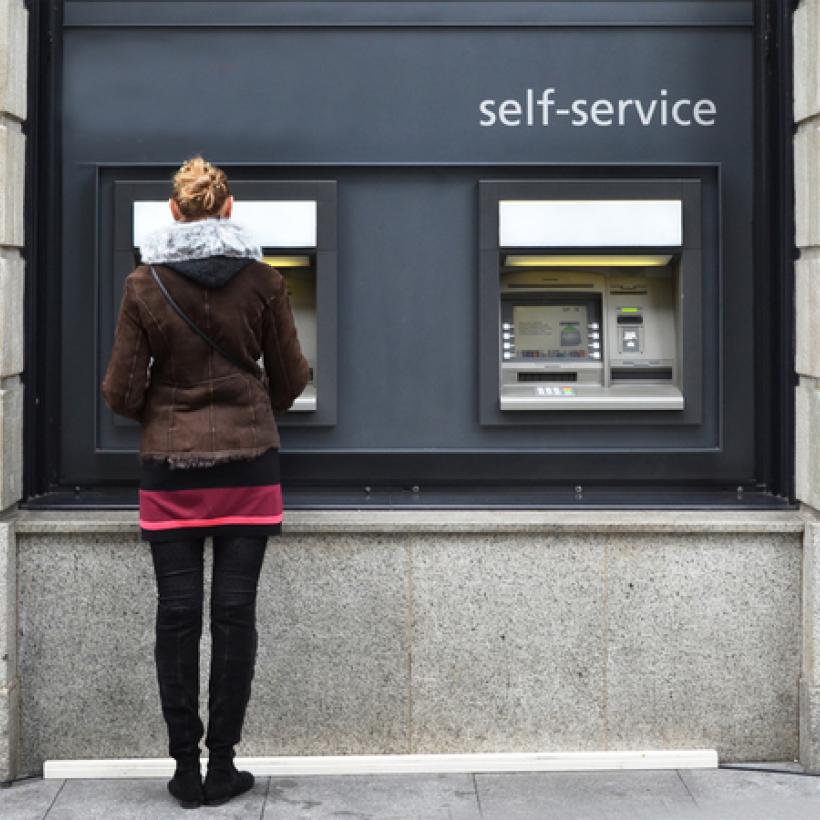 Une femme se tient debout de dos devant un distributeur de billet.