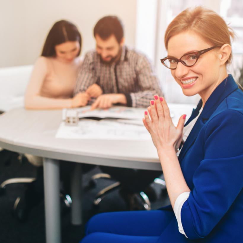 Une femme travaillant pour une compagnie d'assurance se frotte les mains pendant qu'un couple naïf signe un contrat.