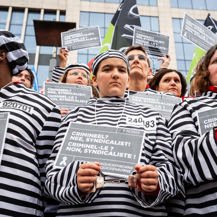 Actie tegen de anti-betogingswet in 2023. Actievoerders in gevangenisplunje houden bordjes vast: “Crimineel? Nee, syndicalist”