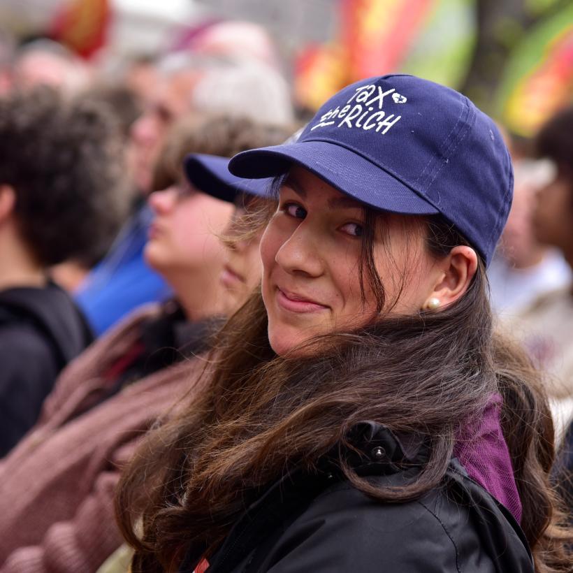 Une jeune femme avec une casquette « Tax The Rich ».