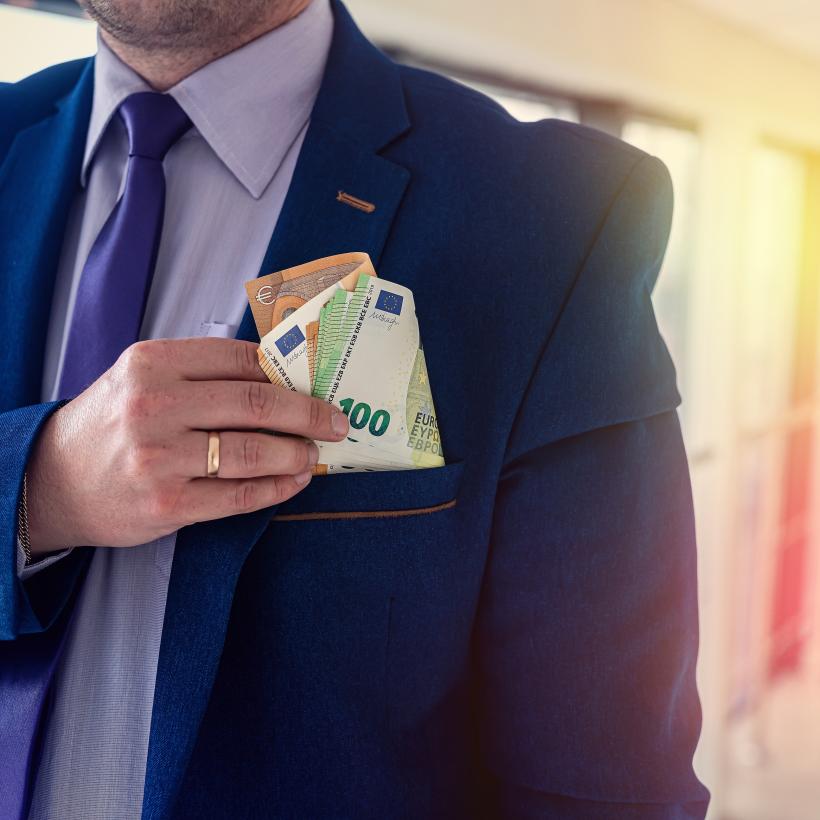 Un homme en costume met une liasse de billets dans sa poche