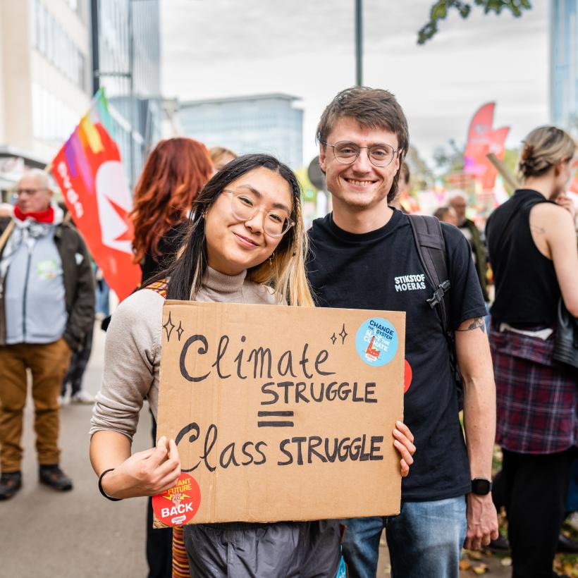 Un jeune homme et une jeune femme à une manifestation porte une pancarte "Climate struggle = class struggle"