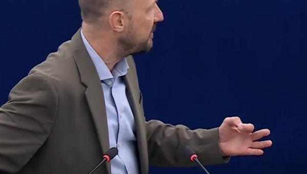Marc Botenga in het Europees parlement terwijl hij zich omkeert en zich boos maakt op de lachende ministers achter hem