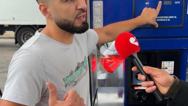Un jeune homme montre du doigt le prix indiqué par la pompe à essence